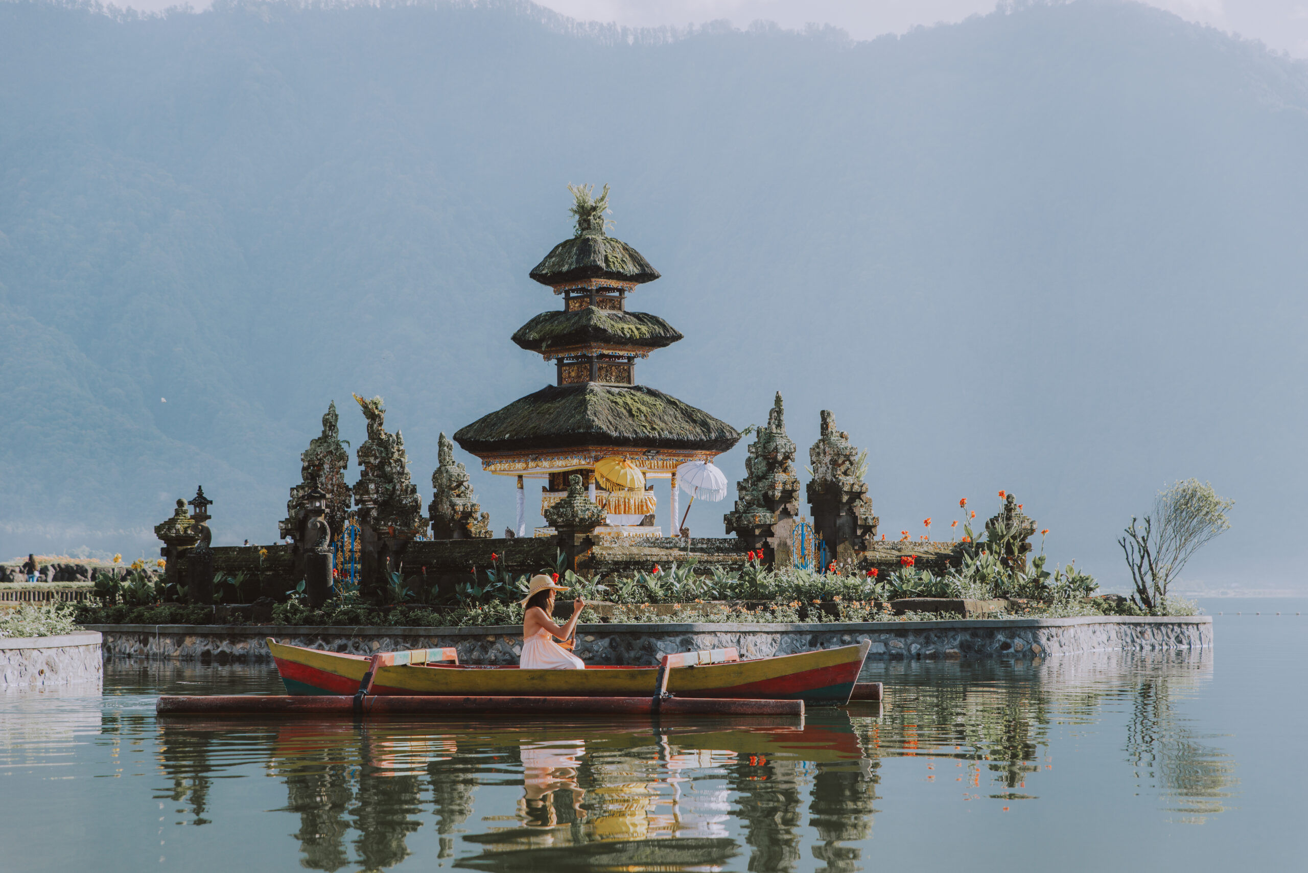 Young woman traveler paddling on a wooden boat at Pura Ulun Danu